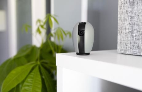 كاميرا مراقبة بيضاء بتصميم أنيق موضوعة على رف خشبي