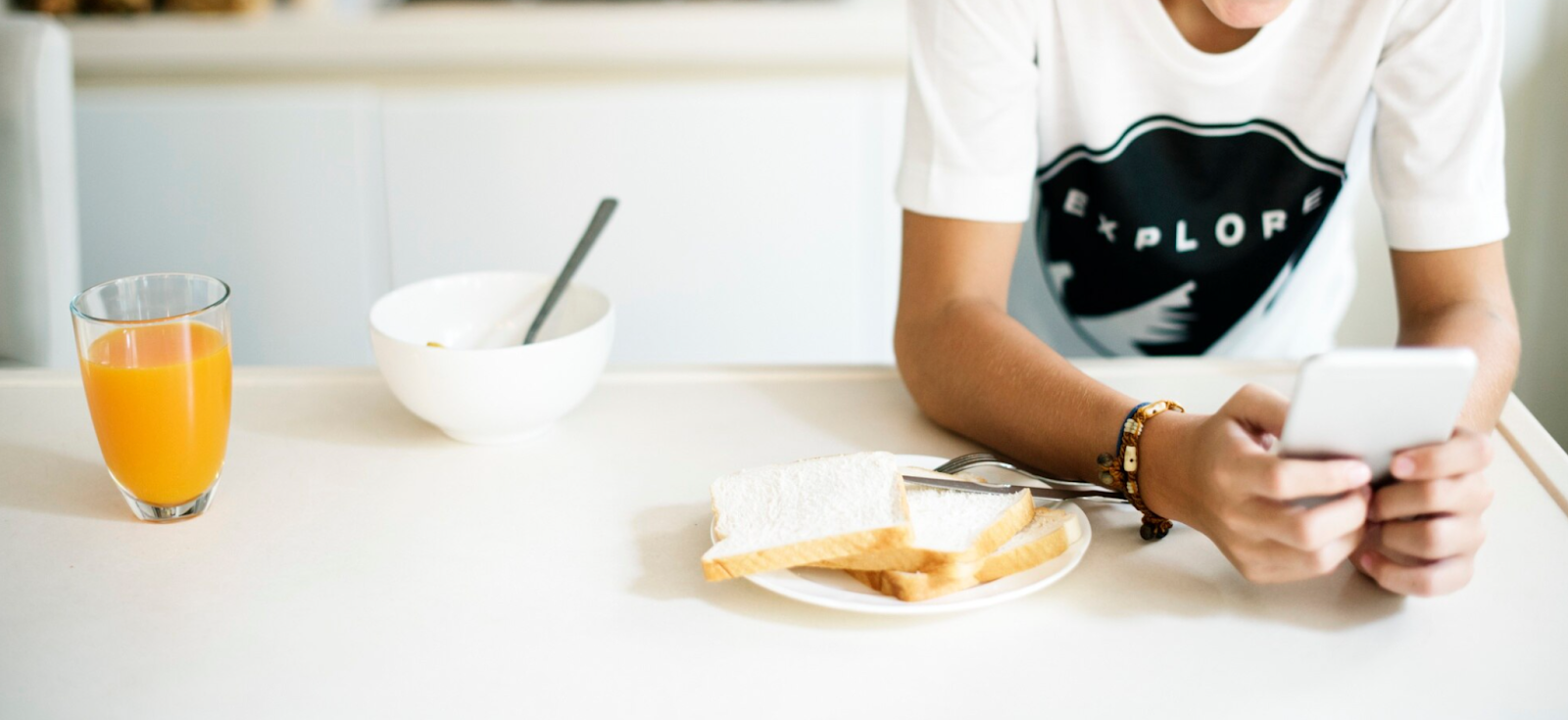 A young person enjoying a healthy breakfast of toast and orange juice while using a tablet.
